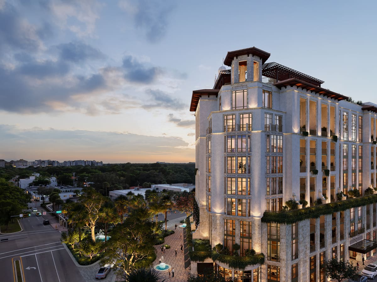 The Ponce Park Residences façade at twilight above the Coral Gables treeline, terraces glowing along its full height