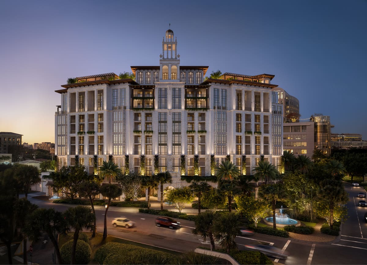 Ponce Park Residences Coral Gables seen from Ponce de Leon Boulevard at dusk, its neoclassical limestone façade and corner tower lit from within